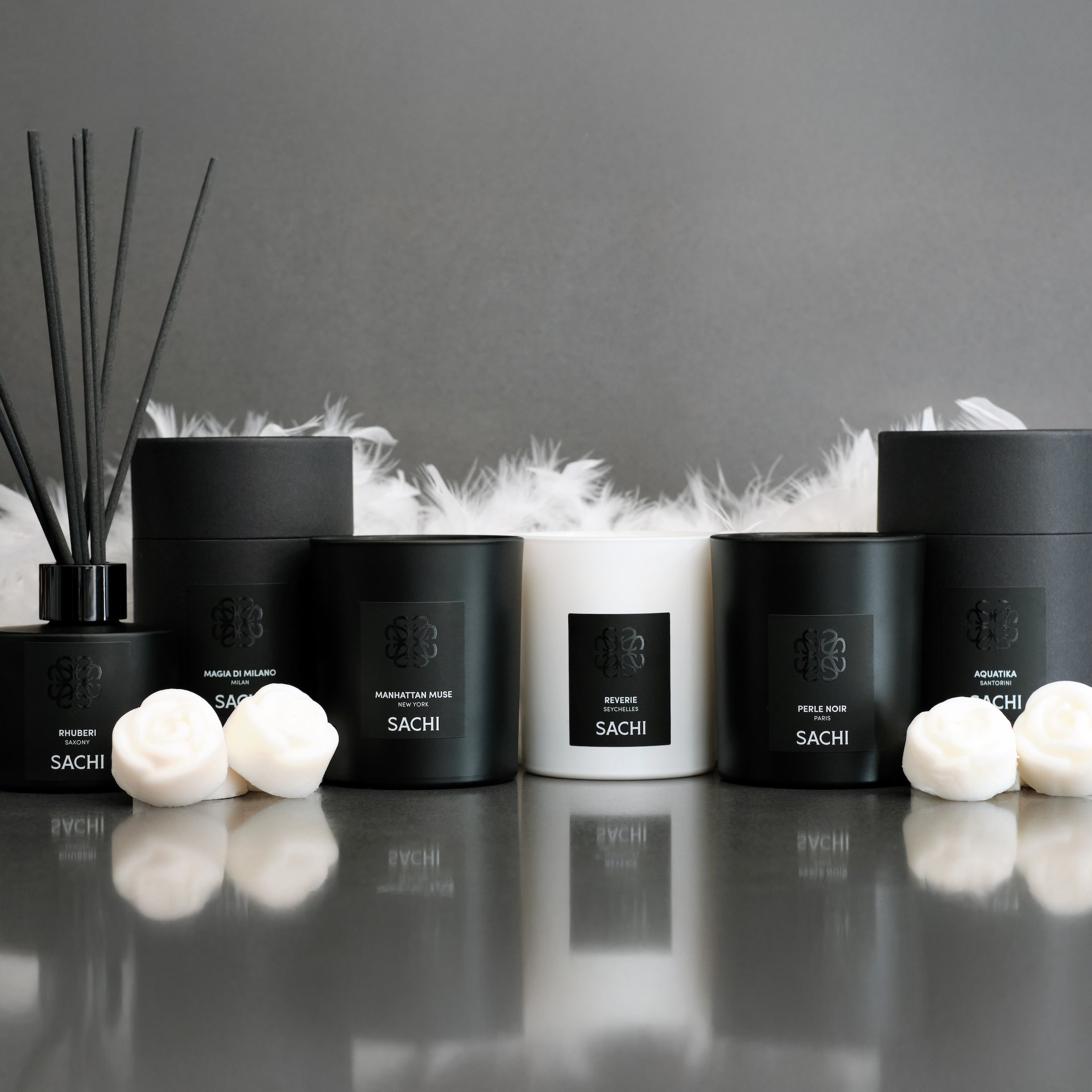 SACHI candles and diffusers on a reflective surface with a grey background